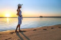 Young woman in straw hat and a dress walking alone on empty sand beach at sunset sea shore. Lonely girl looking at horizon over Royalty Free Stock Photo