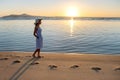 Young woman in straw hat and a dress walking alone on empty sand beach at sunset sea shore. Lonely girl looking at horizon over Royalty Free Stock Photo