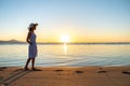 Young woman in straw hat and a dress walking alone on empty sand beach at sunset sea shore. Lonely girl looking at horizon over Royalty Free Stock Photo