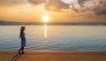 Young woman in straw hat and a dress walking alone on empty sand beach at sunset sea shore. Lonely girl looking at horizon over Royalty Free Stock Photo