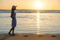 Young woman in straw hat and a dress walking alone on empty sand beach at sunset sea shore. Lonely girl looking at horizon over Royalty Free Stock Photo