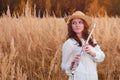 A young woman in straw hat with red hair plays a flute in an autumn field. A musician with a wind instrument in the tall grass