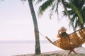 A young woman in straw hat sitting in a hammock swinging between a palm trees on the overseas island sand beach at sunrise time. Royalty Free Stock Photo