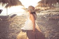 Young woman in straw hat sitting on a tropical beach, enjoying sand and sunset. Laying in the shade of palm tree parasols Royalty Free Stock Photo