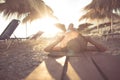 Young woman in straw hat sitting on a tropical beach,enjoying sand and sunset.Laying in the shade of palm tree parasols Royalty Free Stock Photo