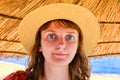 A young woman in a straw hat stands under an umbrella. Girl on the evening beach near the blue sea. Female face, close-up Royalty Free Stock Photo