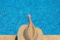 Young woman in straw hat sunbathing sitting on the edge of swimming pool with legs in water Top view Royalty Free Stock Photo