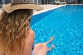 Young woman in straw hat sunbathing sitting on the edge of swimming pool with legs in water