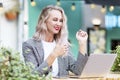 Young woman in a street cafe with a laptop. A beautiful blonde with long hair smiles and gestures. Blogging, remote work and