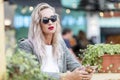 Young woman in a street cafe with a phone. A beautiful blonde with long hair in business clothes and sunglasses. Blogging, remote