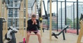 Young woman strengthening legs with fitness band on sports ground. Physical training. Healthy lifestyle. Outdoor