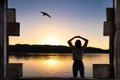 Young woman stretching arms under the sunrise at lake with wooden framing