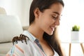 Young woman with striped knee tarantula on shoulder at home
