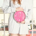 Young woman in striped shirt holding pink alarm clock