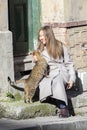 Young woman strokes a stray cat near a house.