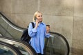 Young woman, student on escalator, drinking coffee and answer to phone call, talking with someone and smiling Royalty Free Stock Photo