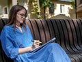 Young woman student in eyewear sitting on bench in public park with syllabus or textbook with highlighter. Female Royalty Free Stock Photo