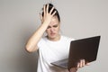 Young woman student looks at her laptop, she is confused and worried about solving a problem, holds her palm on her forehead and Royalty Free Stock Photo