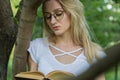 Young woman student reading a book leaning on a tree in the park Royalty Free Stock Photo