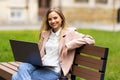 Young woman student sitting on a bench in the park and typing on her laptop on a sunny day Royalty Free Stock Photo