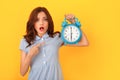 Young woman studio isolated on yellow holding alarm clock pointing at time Royalty Free Stock Photo