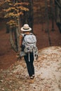 Young woman in a stylish hat and travel bag on her shoulders, looking around at the charming autumn forest Royalty Free Stock Photo