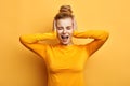 Young woman in stylish yellow sweater screaming in terror with hands on her ears Royalty Free Stock Photo