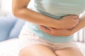 Young woman suffering from abdominal pain while sitting on the sofa and feeling stomach ache, symptom of pms