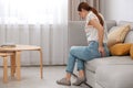 Young woman suffering from hemorrhoid on sofa