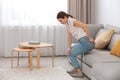 Young woman suffering from hemorrhoid on sofa