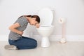 Young woman suffering from nausea at toilet bowl indoors