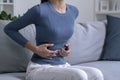 Young woman suffering from strong abdominal pain while sitting on sofa at home Royalty Free Stock Photo