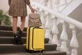 Young woman with suitcase and stylish backpack going up stairs in hotel, closeup