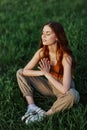 A young woman in summer clothes sitting on the green grass doing yoga and meditating in nature, a connection with the Royalty Free Stock Photo