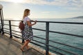 Young woman in summer dress and protective mask on face, standing on deserted pier and looks at sea Royalty Free Stock Photo