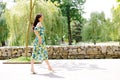 Young woman in summer dress is walking in green park and enjoying the sun. Playful and beautiful girl on warm sunny day Royalty Free Stock Photo