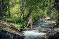 Young woman in a summer dress walking on a wooden bridge over mountain stream. Excursion in nature reserve. Picturesque forest Royalty Free Stock Photo