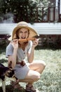 Young funny woman in summer hat grilling meat outdoors in the backyard, sitting with her dog Royalty Free Stock Photo