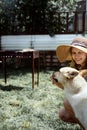 Young woman in summer hat grilling meat outdoors in the backyard, sitting with her dog Royalty Free Stock Photo