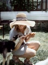 Young woman in summer hat grilling meat outdoors in the backyard, sitting with her dog Royalty Free Stock Photo