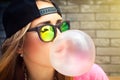 Woman in sunglasses and a cap makes a chewing gum bubble Royalty Free Stock Photo