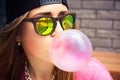 Woman in sunglasses and a cap makes a chewing gum bubble Royalty Free Stock Photo