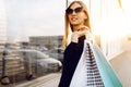 Young woman in sunglasses and dress, with shopping bags, in the city against the background of a shopping center Royalty Free Stock Photo