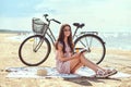 Young woman in sunglasses holds a book and looking at camera while sitting on the beach. Royalty Free Stock Photo