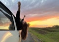 Young woman in sunglasses looks out of the window of a white car. Pretty female brunette opened her arms to the sky Royalty Free Stock Photo