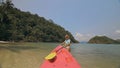 Young woman in sunglasses pulls pink plastic canoe with paddle to azure sea water from beach with palms. Royalty Free Stock Photo