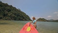 Young woman in sunglasses pulls pink plastic canoe with paddle to azure sea water from beach with palms. Royalty Free Stock Photo