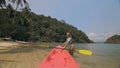 Young woman in sunglasses pulls pink plastic canoe with paddle to azure sea water from beach with palms. Royalty Free Stock Photo