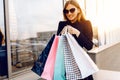 Young woman in sunglasses and dress, with shopping bags, in the city against the background of a shopping center at sunset Royalty Free Stock Photo