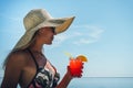 A young woman in sunglasses and a straw hat holds a cocktail in her hand against the blue sky and sea. Beautiful girl is drinking Royalty Free Stock Photo